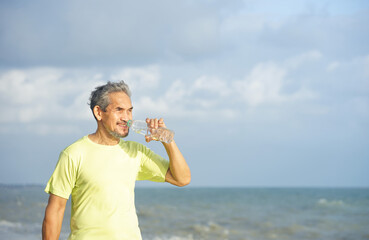 senior man drinking water after workout on the beach......