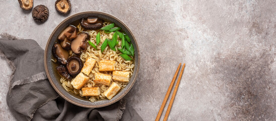 Asian vegan ramen noodle soup with roasted tofu cheese and shiitake mushrooms in a bowl on brown...