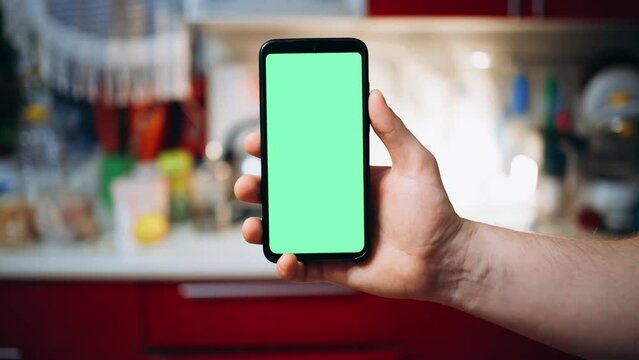 a man holds a phone with a green screen in his hands in the background of the kitchen
