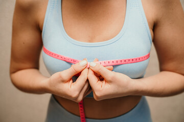 Cropped view of slim woman measuring breasts with tape measure at home, close up. Unrecognizable...