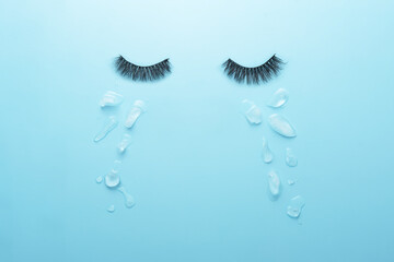 Creative concept of sadness. Glued lashes on a blue background with tears in the form of ice pieces.