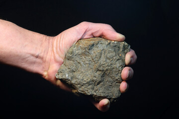 Hand holding a large stone on black background.