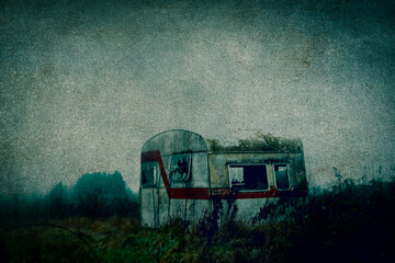 An abandoned, broken caravan in the countryside on a moody winters day. With a grunge, grainy edit.