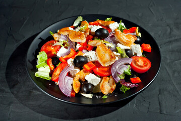 Salad with tomatoes, peppers, olives and chicken fillet. Fresh salad in a black plate on a dark background.