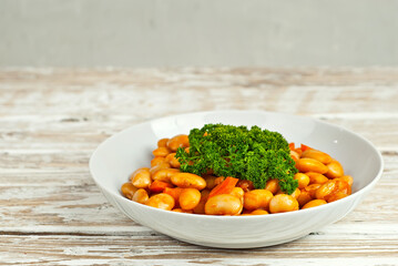 Beans with carrots in a white bowl. Beans on a white background. Food on a shabby table. Bowl on an old wooden board.