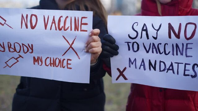 Front view anti vax placards in female Caucasian hands on spring autumn day outdoors. Unrecognizable women protesting against mandatory coronavirus vaccination. Freedom concept