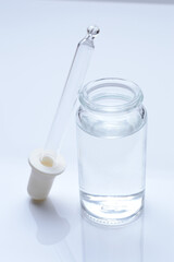 Fototapeta na wymiar glass transparent jar and a cosmetic pipette with liquid droplets on a white background.