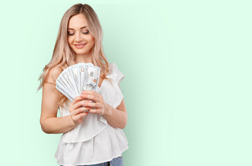Young happy woman with dollar banknotes in hand isolated on color background