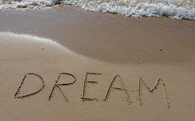 the inscription DREAM on the sand of the coastline