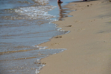 Footprints of a man on the yellow beach sand from walking barefoot by the sea with water that washes away the footprints.