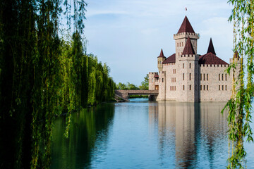 Fototapeta premium The castle stands on a blooming green lake, surrounded by a beautiful park area.