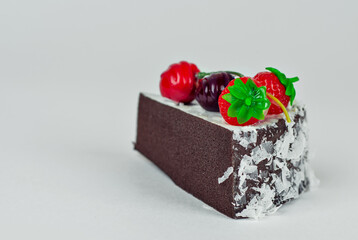 A piece of brown cake on a white background. Cake with strawberries and cherries close up.