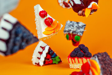 Various cakes fall on an orange background. Glazed triangular pieces of cake with chocolate filling and fruit creams. Sweets fly in the air.