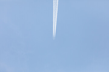 Weit entferntes Flugzeug mit Kondensstreifen vor blauem Himmel