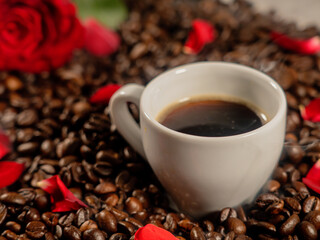 Coffee in a white cup on coffee beans and rose petals with a red rose.The concept of congratulations, Valentine's Day, mother's day