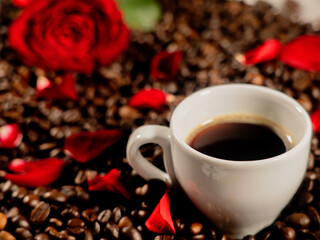 Coffee in a white cup on coffee beans and rose petals with a red rose.The concept of congratulations, Valentine's Day, mother's day