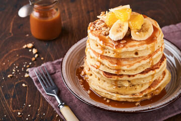 Pancakes. Homemade fluffy pancake with banana, walnut and caramel for breakfast on dark wooden background. Delicious pancakes for traditional American breakfast. Selective focus. Mock up.