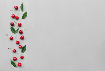 Flat lay top view on gray concrete background with sweet cherry berries and green leaves. Freshness, summer conceptual minimal background. Eco, bio farm food and fruits concept with copy space area
