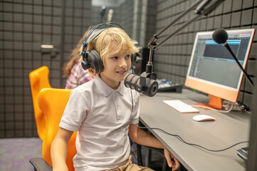 Pleased boy concentrated on recording a podcast in the studio