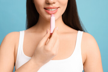 Young woman applying lip balm on turquoise background, closeup