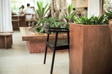 Selective focus on a wooden chair behind the wooden counter with blurred indoor plantation and people in background