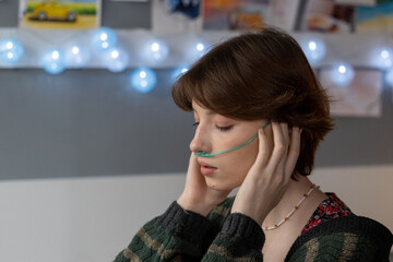 Sick teenage girl with oxygen nose pipe touching temples while suffering from headache in hospital...