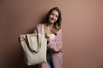 Happy young woman with blank eco friendly bag against light brown background