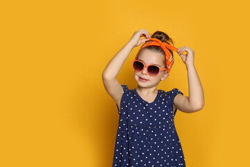 Cute little girl wearing stylish bandana and sunglasses on orange background, space for text