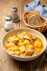 Meat stew with potato and carrot in bowl on wooden background