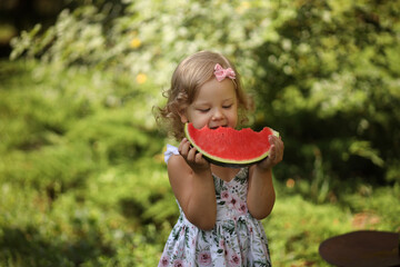 A cute little blonde girl eats a fresh red watermelon in the summer on the street. High-quality photography