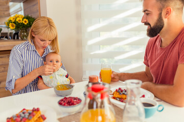 Obraz na płótnie Canvas Parents feeding baby boy while having breakfast