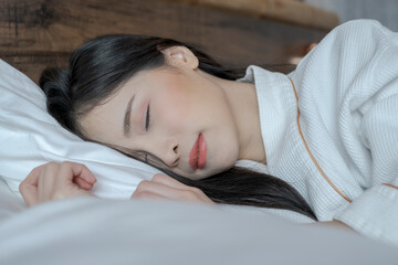 Obraz na płótnie Canvas Young Asian woman with lying in bed under white cover in the morning. Young pretty lady sleeping in bed. Young woman on bed in modern apartment. Woman stretching in bed after wake up.