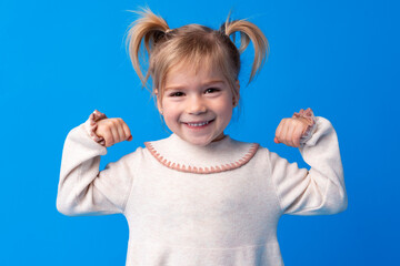 Little cute girl showing her strength against blue background