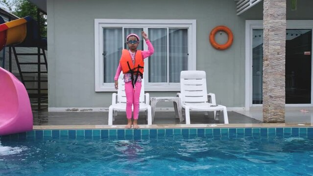Asian girl in a pink bathing suit is jumping in the swimming pool having fun.