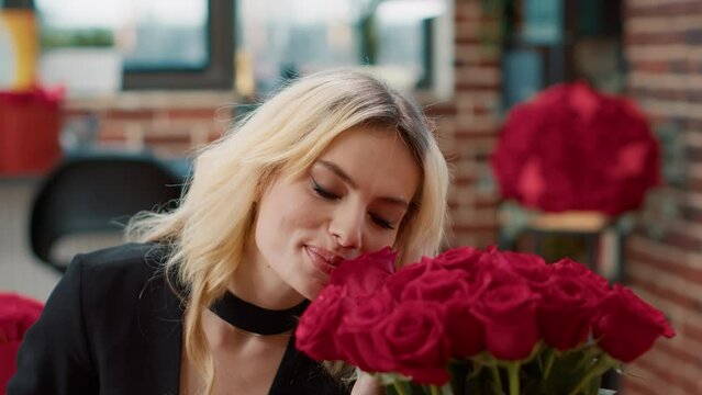 Portrait of romantic beautiful woman smiling and smelling roses feeling in love admiring luxury gift bouquet of roses in living room. Seductive blonde passionate about recieving valentine day flowers.