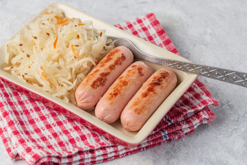 The traditional dish is fried sausages and sauerkraut salad in a red rectangular plate with fork on a napkin on light table