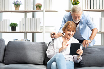 senior couple, elderly man and woman using tablet and say hello to someone on sofa