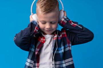 Portrait of a cute little kid in headphones listening to music over blue background