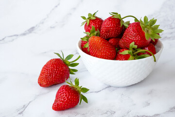Delicious juicy strawberries in white bowl on marble background. Healthy eating, raw diet and detox food concept. Farm strawberry harvest.