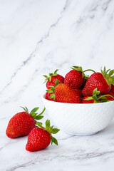 Delicious juicy strawberries in white bowl on marble background. Healthy eating, raw diet and detox food concept. Farm strawberry harvest.