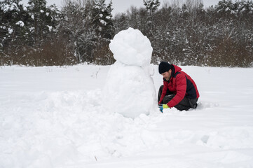 Fototapeta na wymiar A man makes a snowman in a snow-covered field in the open air. Winter time