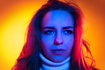 Closeup young beautiful girl looking at camera isolated on orange background in neon light, filter. Concept of emotions