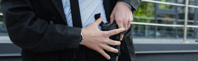 partial view of security man taking gun out of holster outdoors, banner.