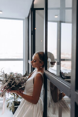 Bride with a wedding bouquet at the window. Wedding preparations. Bride morning.