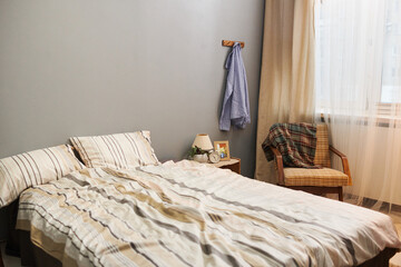 Double bed with two pillows and striped bedcloth, armchair with checkered plaid by window and other stuff in bedroom