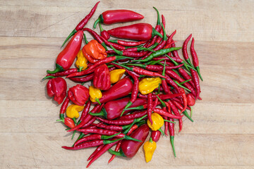 Mixed red, green, orange and yellow hot chili peppers on a wooden table