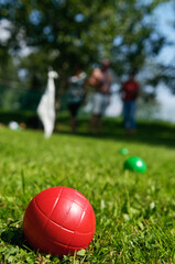 Close-up of red boccia ball lying in grass and people playing in background
