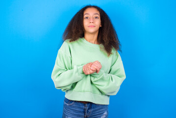 Fototapeta na wymiar Photo of cheerful confident beautiful teenager girl wearing green sweater standing against blue background arms together