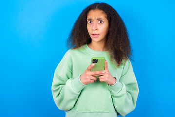 Photo of astonished crazy beautiful teenager girl wearing green sweater standing against blue...
