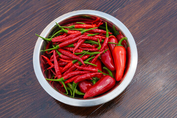 Mixed red hot chili peppers in bowl on a wooden table